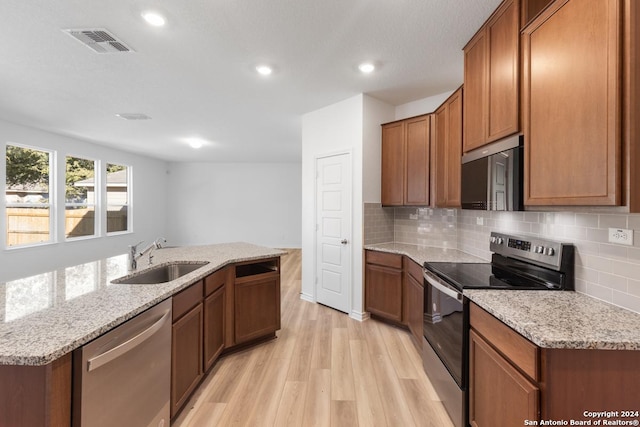 kitchen featuring light stone counters, sink, stainless steel appliances, and a kitchen island with sink