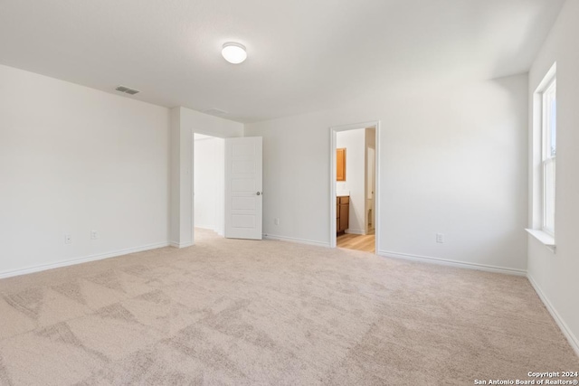 unfurnished bedroom with ensuite bathroom and light colored carpet