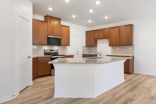 kitchen with sink, light stone counters, electric range, an island with sink, and light hardwood / wood-style floors