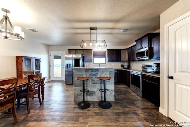 kitchen featuring a notable chandelier, dark brown cabinets, hanging light fixtures, a center island, and appliances with stainless steel finishes