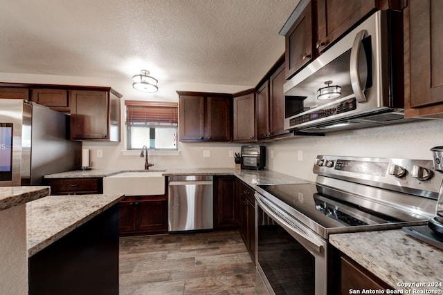 kitchen with hardwood / wood-style floors, sink, light stone counters, dark brown cabinetry, and appliances with stainless steel finishes