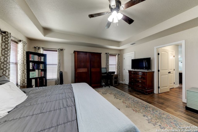 bedroom featuring a tray ceiling, multiple windows, dark hardwood / wood-style floors, and ceiling fan