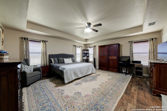 bedroom featuring dark hardwood / wood-style floors, a textured ceiling, a raised ceiling, and ceiling fan