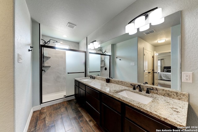 bathroom featuring hardwood / wood-style floors, a shower with door, a textured ceiling, and dual bowl vanity