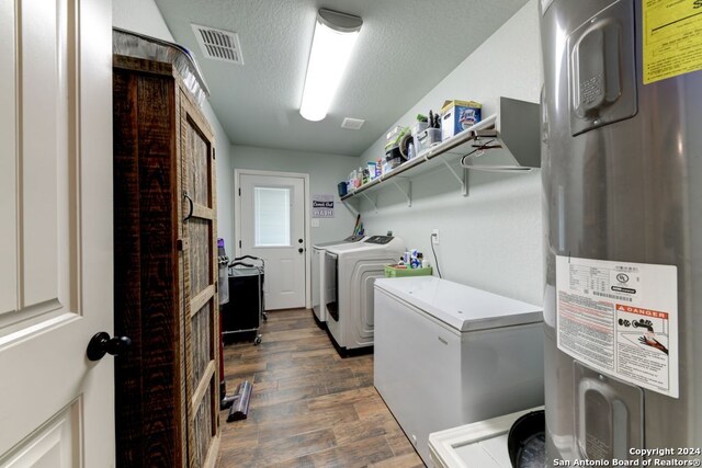 laundry room featuring electric water heater, washing machine and dryer, a textured ceiling, and dark hardwood / wood-style flooring