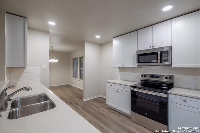 kitchen with sink, white cabinetry, hanging light fixtures, appliances with stainless steel finishes, and light hardwood / wood-style floors