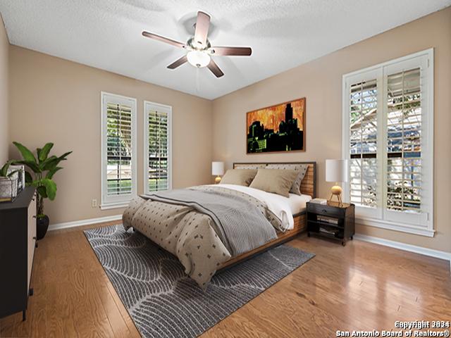 bedroom featuring ceiling fan, wood-type flooring, multiple windows, and a textured ceiling