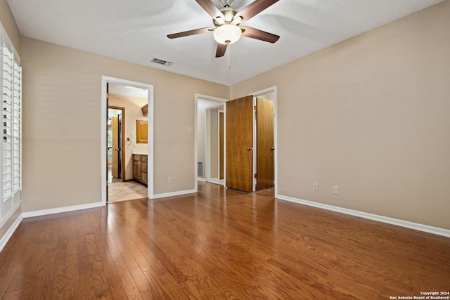 unfurnished bedroom with ceiling fan, wood-type flooring, connected bathroom, and a textured ceiling