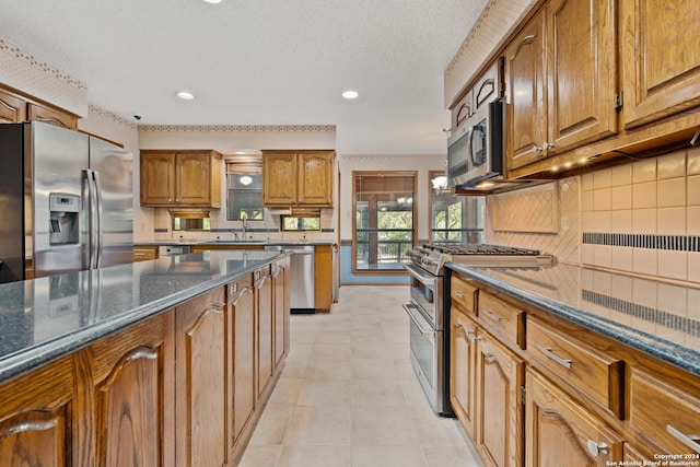 kitchen featuring sink, a textured ceiling, appliances with stainless steel finishes, dark stone counters, and backsplash