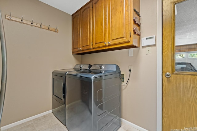 laundry room with cabinets, a textured ceiling, washer and dryer, and light tile patterned floors