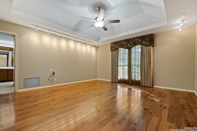 empty room featuring a tray ceiling, ceiling fan, light hardwood / wood-style floors, track lighting, and a textured ceiling