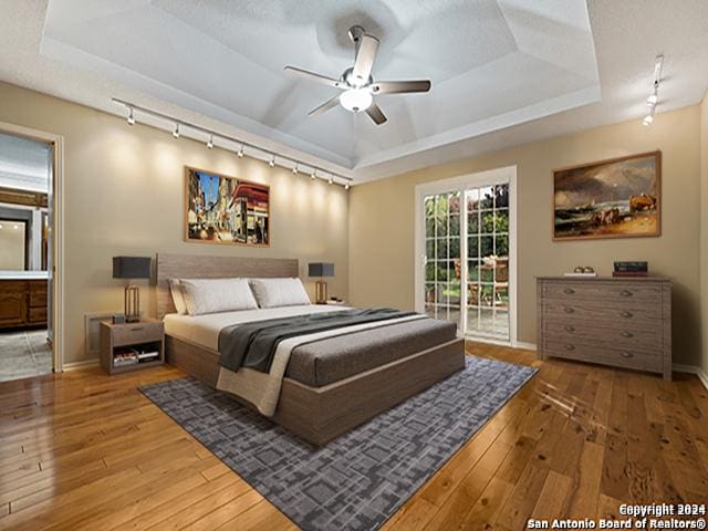 bedroom featuring access to outside, track lighting, a raised ceiling, hardwood / wood-style flooring, and ceiling fan