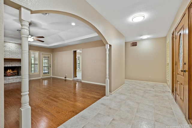 foyer with a brick fireplace, a textured ceiling, ceiling fan, and light hardwood / wood-style flooring