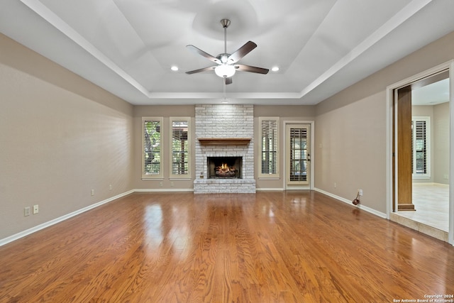 unfurnished living room featuring ceiling fan, wood-type flooring, a fireplace, and a tray ceiling