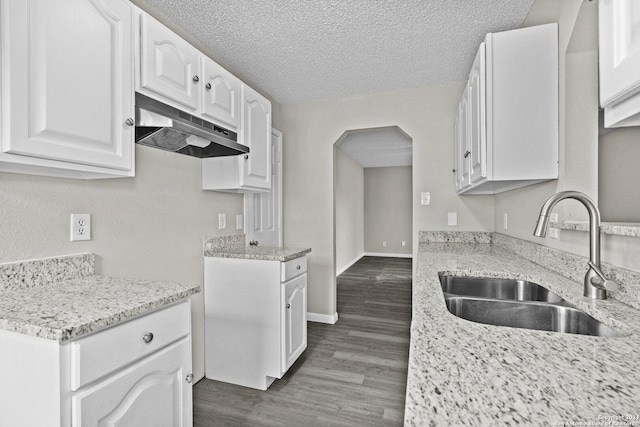 kitchen featuring under cabinet range hood, a sink, a textured ceiling, dark wood finished floors, and white cabinets