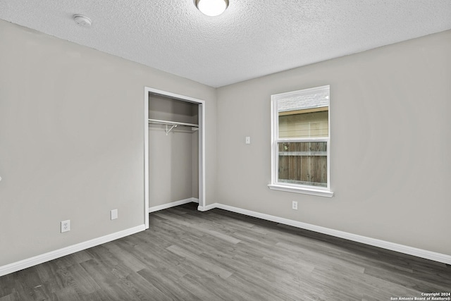 unfurnished bedroom featuring wood finished floors, baseboards, a closet, and a textured ceiling