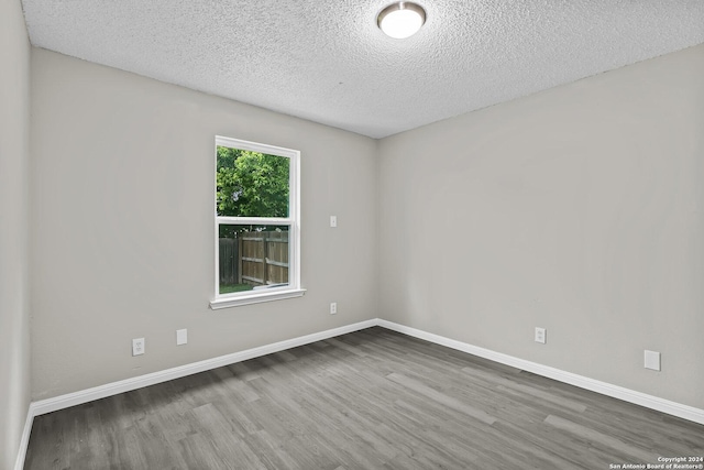 empty room with a textured ceiling, baseboards, and wood finished floors