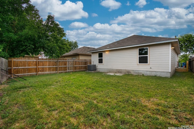 rear view of house featuring a lawn, central AC, and a fenced backyard