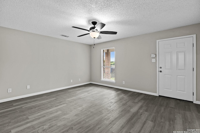 empty room with dark wood-style floors, visible vents, baseboards, ceiling fan, and a textured ceiling