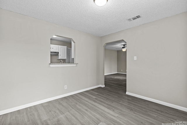 spare room featuring wood finished floors, visible vents, baseboards, arched walkways, and a textured ceiling