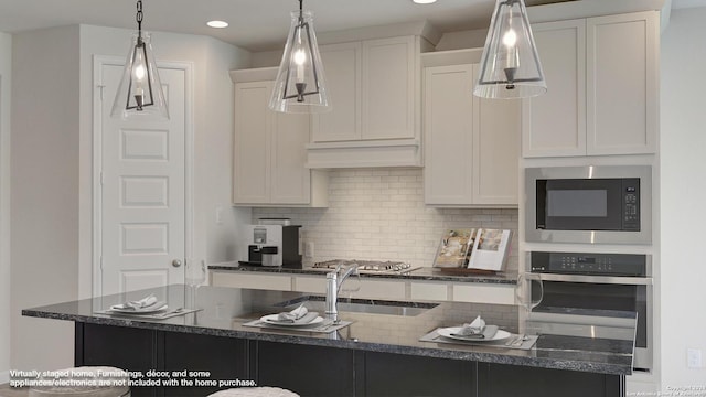 kitchen with appliances with stainless steel finishes, tasteful backsplash, an island with sink, white cabinets, and decorative light fixtures