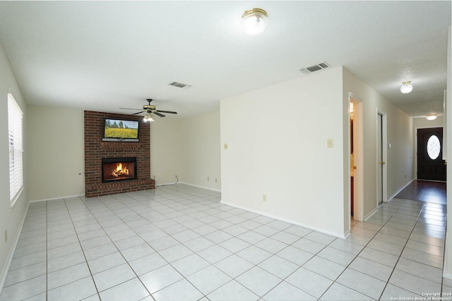 unfurnished living room featuring ceiling fan, a brick fireplace, and light tile patterned floors