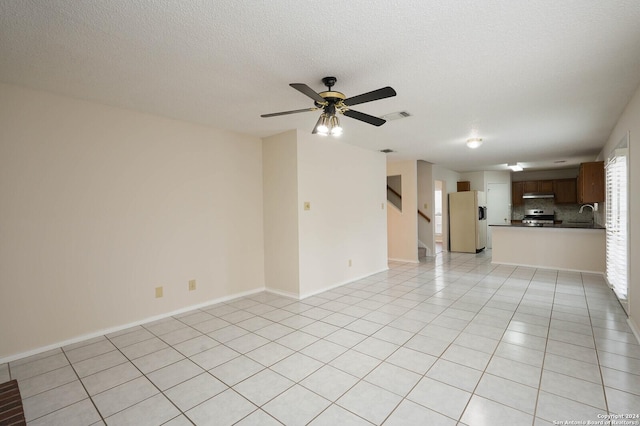 unfurnished living room featuring light tile patterned flooring, ceiling fan, sink, and a textured ceiling