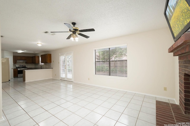 unfurnished living room featuring ceiling fan, a wealth of natural light, a textured ceiling, and light tile patterned floors