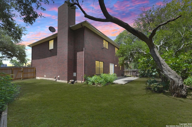 property exterior at dusk featuring a lawn and a patio area