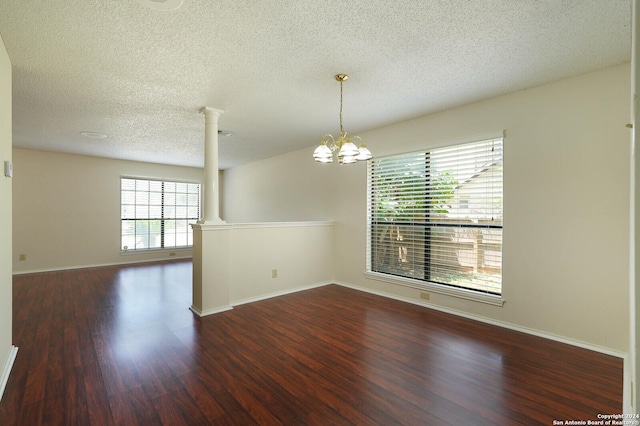 spare room with an inviting chandelier, decorative columns, dark hardwood / wood-style floors, and a textured ceiling