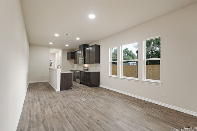 kitchen with an island with sink, light hardwood / wood-style flooring, appliances with stainless steel finishes, and backsplash