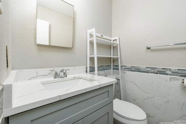 bathroom featuring toilet, a textured wall, tile walls, and vanity