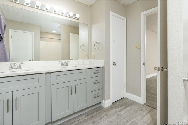 full bathroom with double vanity, baseboards, a sink, and wood finished floors