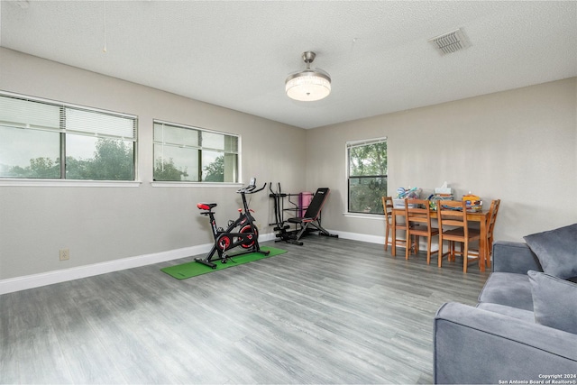 recreation room with a textured ceiling, wood finished floors, visible vents, and baseboards