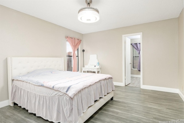 bedroom with ensuite bathroom, wood finished floors, and baseboards