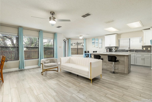 living room featuring plenty of natural light, light wood-style flooring, visible vents, and a textured ceiling