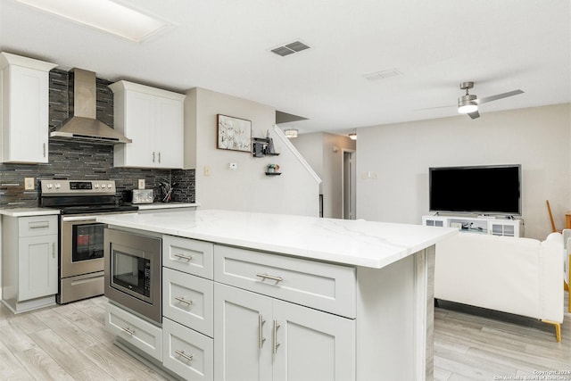 kitchen featuring visible vents, light wood-style floors, appliances with stainless steel finishes, wall chimney range hood, and tasteful backsplash