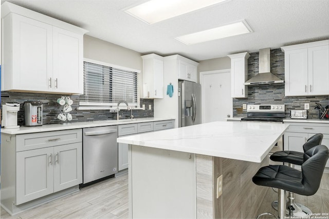 kitchen featuring a center island, wall chimney exhaust hood, tasteful backsplash, appliances with stainless steel finishes, and a kitchen breakfast bar