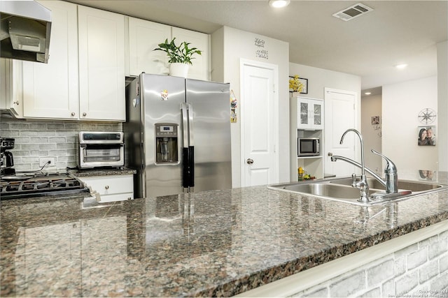 kitchen with tasteful backsplash, ventilation hood, dark stone counters, stainless steel appliances, and white cabinets