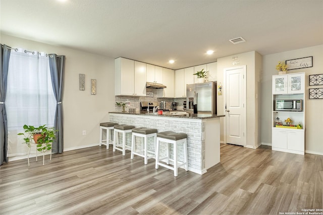 kitchen with stainless steel appliances, white cabinetry, light hardwood / wood-style flooring, and kitchen peninsula