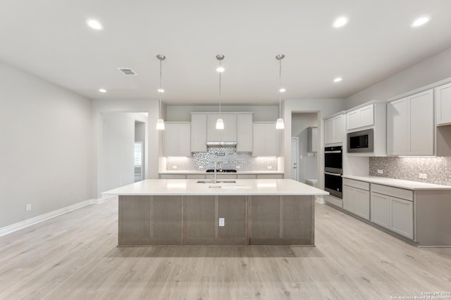 kitchen featuring built in microwave, pendant lighting, light wood-type flooring, and a center island with sink