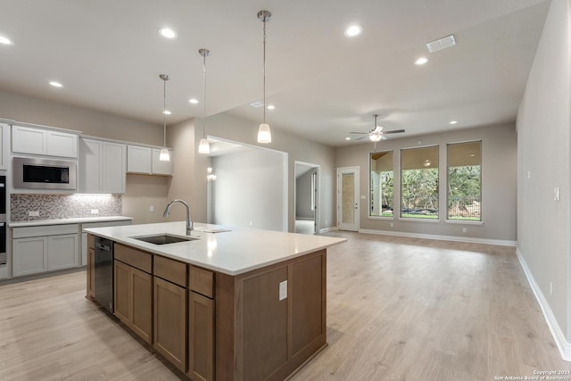 kitchen featuring sink, tasteful backsplash, a center island with sink, stainless steel microwave, and white cabinets