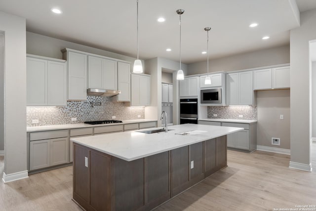 kitchen with sink, decorative light fixtures, a center island with sink, light stone countertops, and black appliances