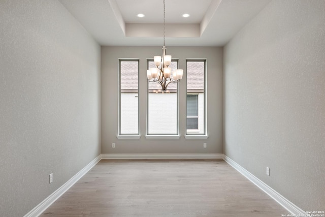 unfurnished dining area with a chandelier, a raised ceiling, and light hardwood / wood-style flooring