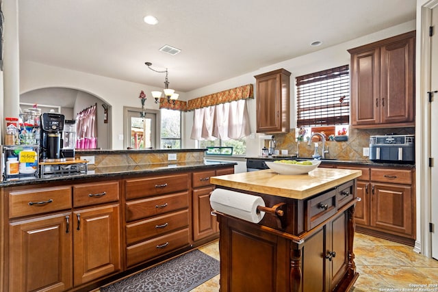 kitchen with butcher block countertops, sink, backsplash, light tile patterned flooring, and a center island