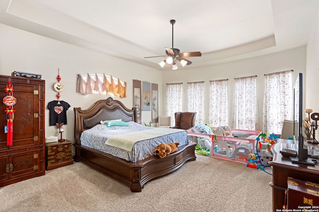 bedroom with a raised ceiling, carpet, and ceiling fan