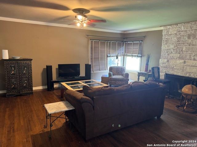 living room featuring crown molding, ceiling fan, a fireplace, and dark wood-type flooring