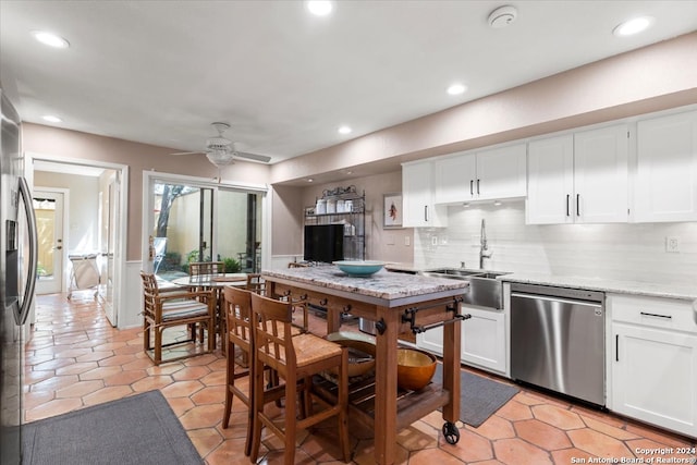 kitchen with light stone counters, ceiling fan, stainless steel dishwasher, decorative backsplash, and sink