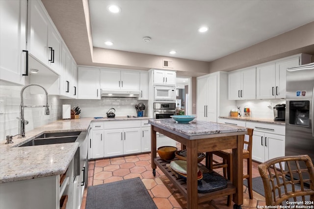 kitchen featuring white cabinetry, tasteful backsplash, light tile patterned floors, light stone counters, and appliances with stainless steel finishes