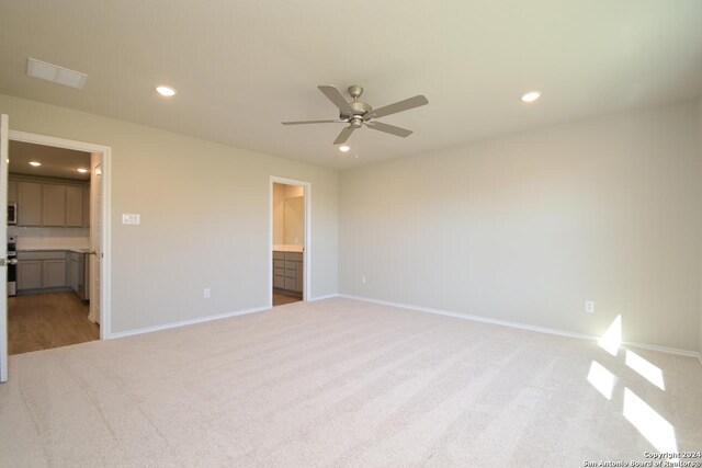 unfurnished bedroom with ceiling fan, ensuite bathroom, and light colored carpet